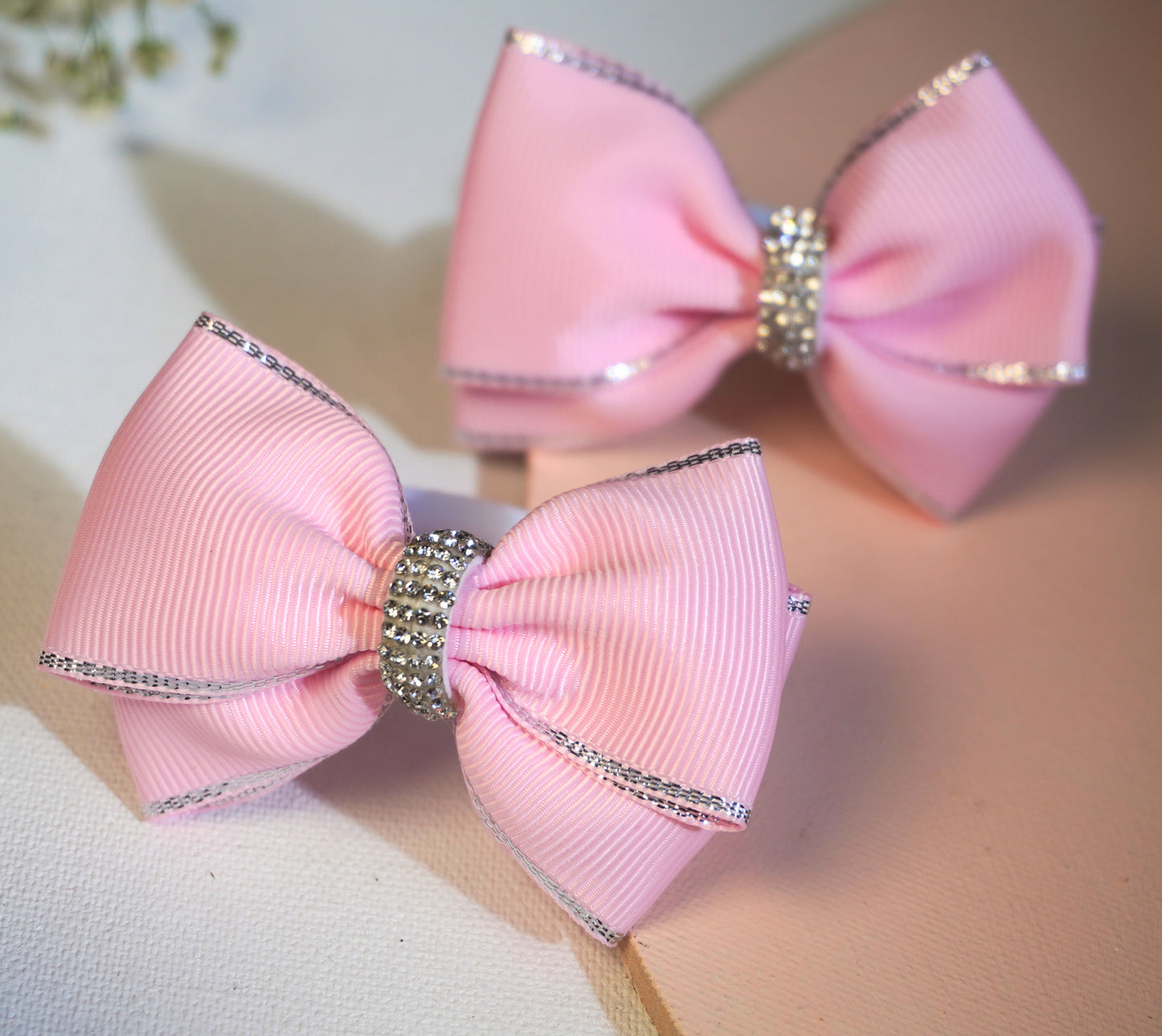 A close-up of a pink grosgrain ribbon hair bow, showing the intricate texture of the high-quality ribbon, the delicate silver metallic edge, and the sparkle of the rhinestone centerpiece.