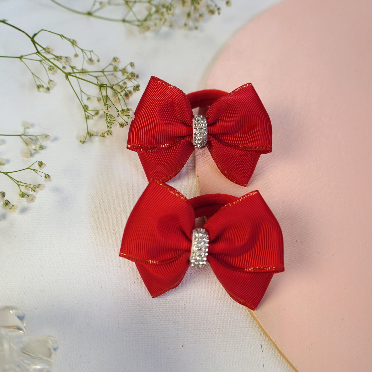 Two red hair bows with rhinestone centers on a light background