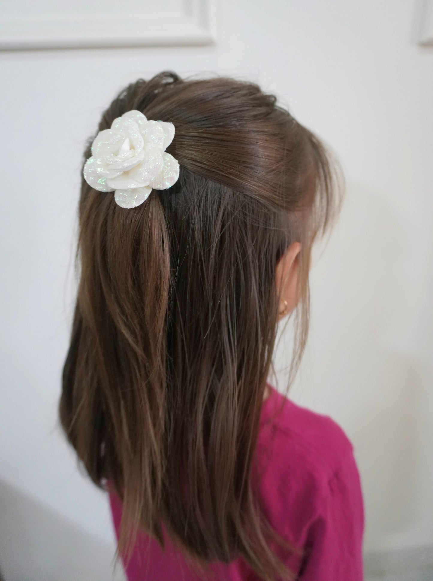 Person with long brown hair wearing a white flower hair clip against a plain background
