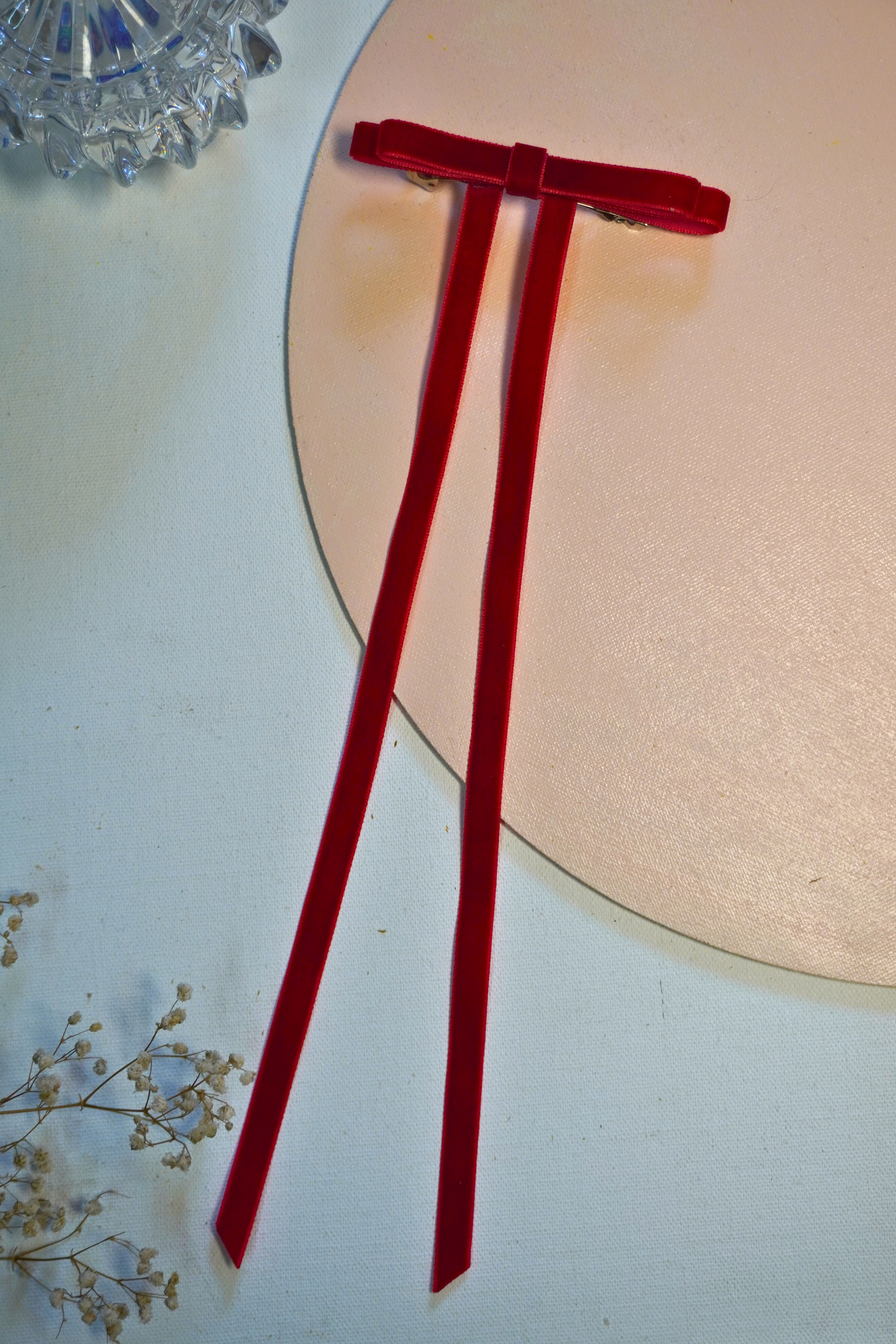 Close-up of the Noel Bow, a deep scarlet premium velvet hair bow with 12-inch long trailing ribbons, styled on a woman with dark voluminous curly hair in a half-updo