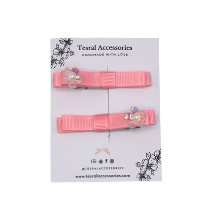 Two pink hair clips with floral accents set on a alligator clip 