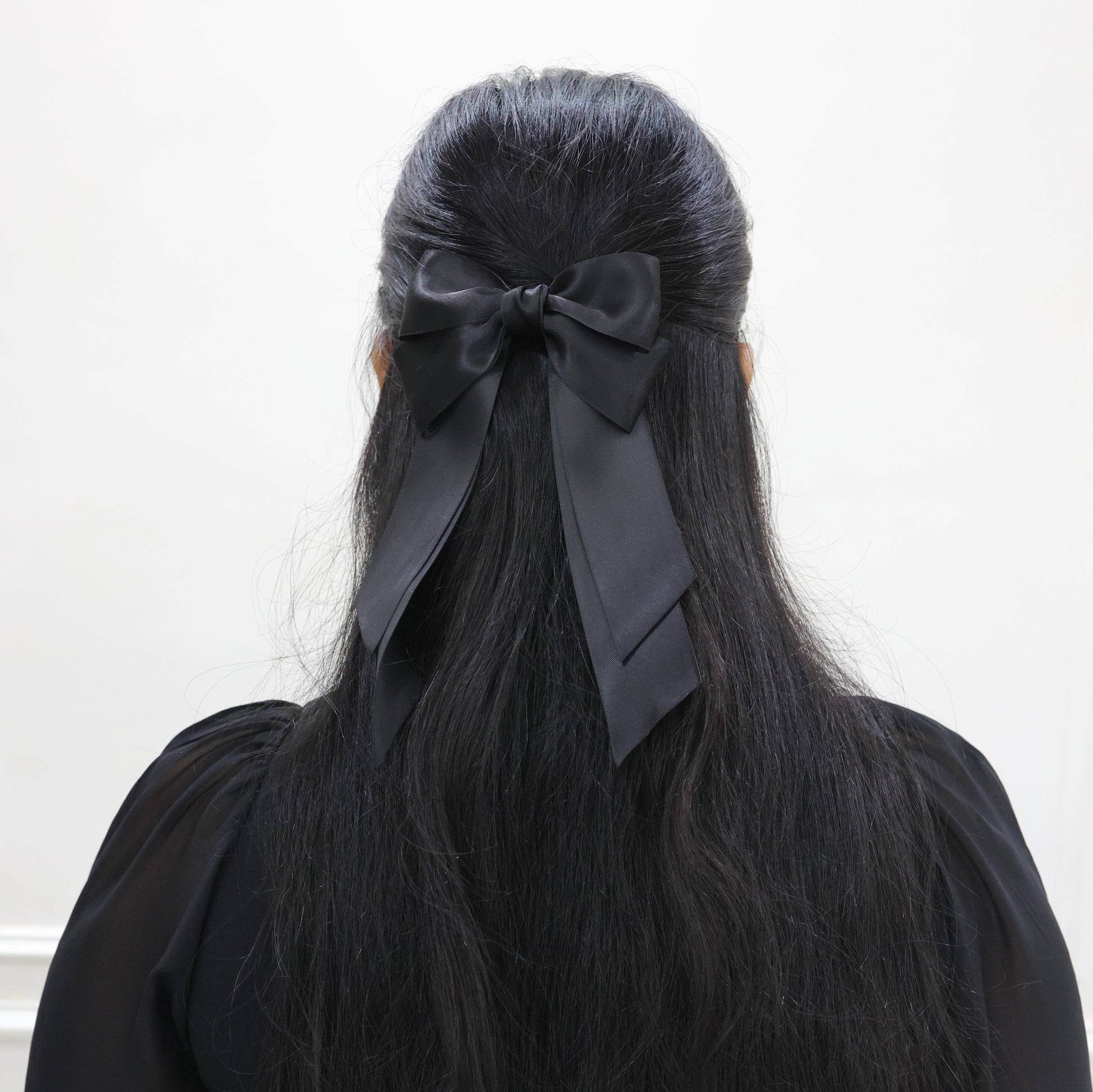 Model wearing Tesral Cascade Black Satin Bow, styled in a sleek half up and half down, showcasing polished finish and versatile elegance.
