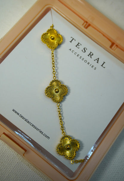 A gold-toned five-cloverchain necklace with central beads, displayed on a white card inside a peach-colored case. The card is branded TESRAL ACCESSORIES.