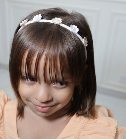 A little girl wearing a peach and white floral headband with pearl accents.