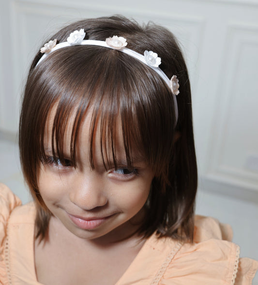 A little girl wearing a peach and white floral headband with pearl accents.
