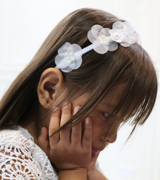 Little girl wearing a white headband with translucent layered petals and delicate pearls.