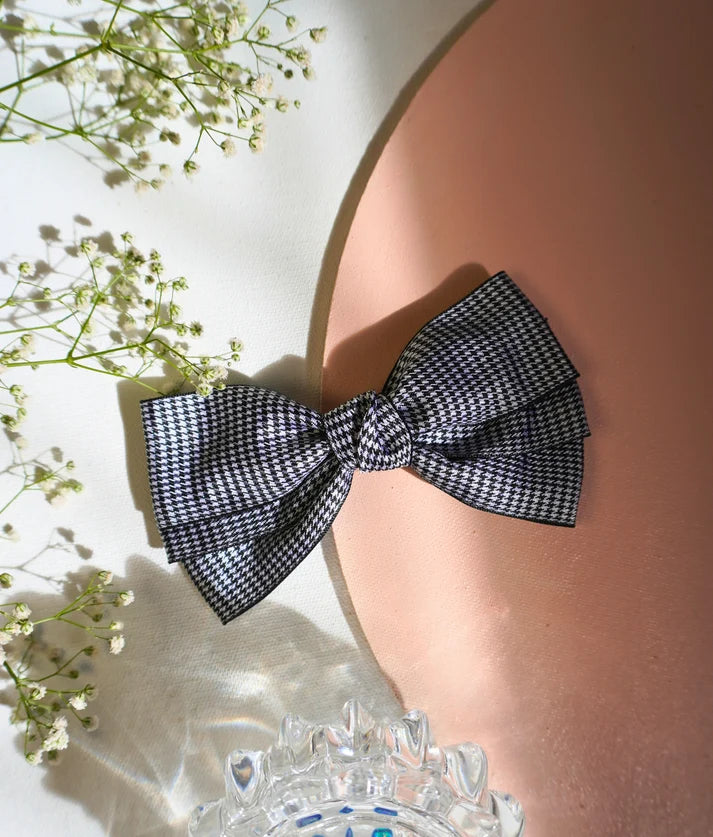 A black and white houndstooth patterned bow tie styled on a split white and peach background with baby's breath flowers and a clear glass dish.