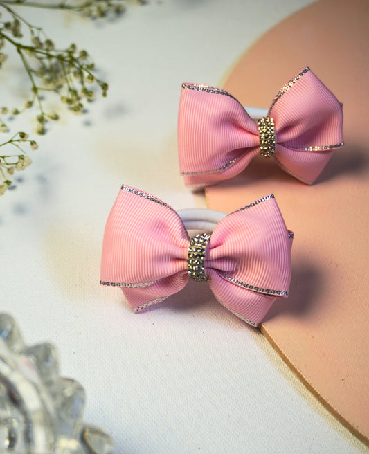 A set of two matching pink grosgrain ribbon hair bows for pigtails, featuring a silver metallic edge and a rhinestone centerpiece. The bows are displayed against a light pink background, perfect for a little girl's party or special occasion.