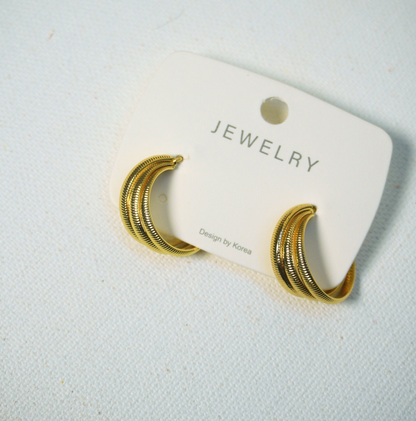 A pair of gold-toned textured hoop earrings attached to a white display card