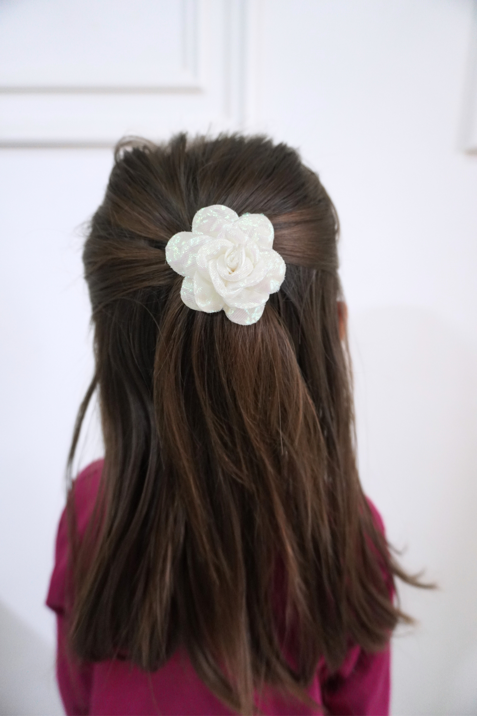 Person with long hair wearing a white flower hair accessory against a white background