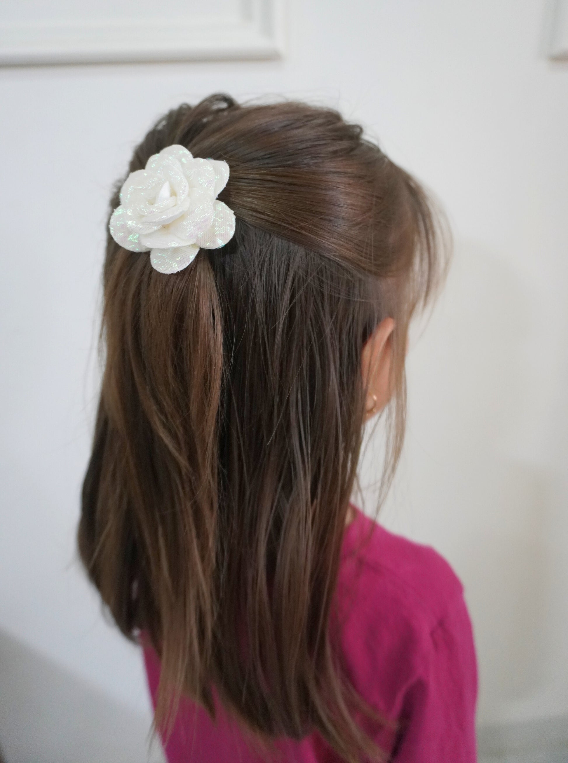 Person with long brown hair wearing a white flower hair clip against a plain background