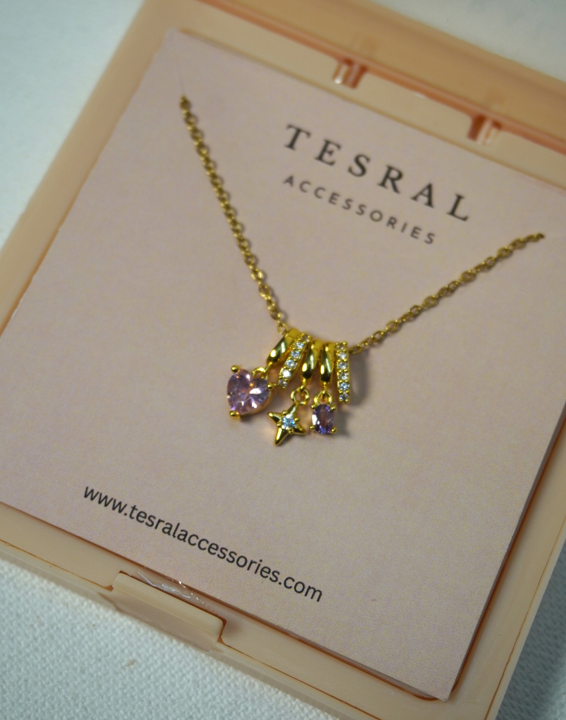 Gold necklace with stacked pendants - heart pendant, purple gemstone, northern star pendant on a Tesral Accessories card.